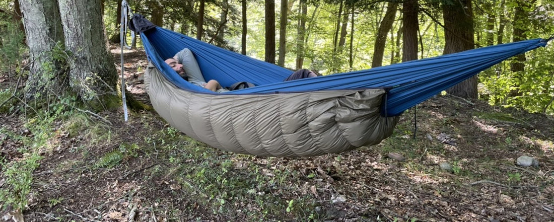 Camper resting in a hammock with a Jacks R Better down underquilt slung below in a summer forest