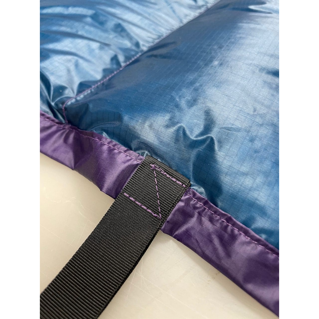 Close-up of a custom quilt's blue shell, purple edge binding, webbing strap, and contrast stitching