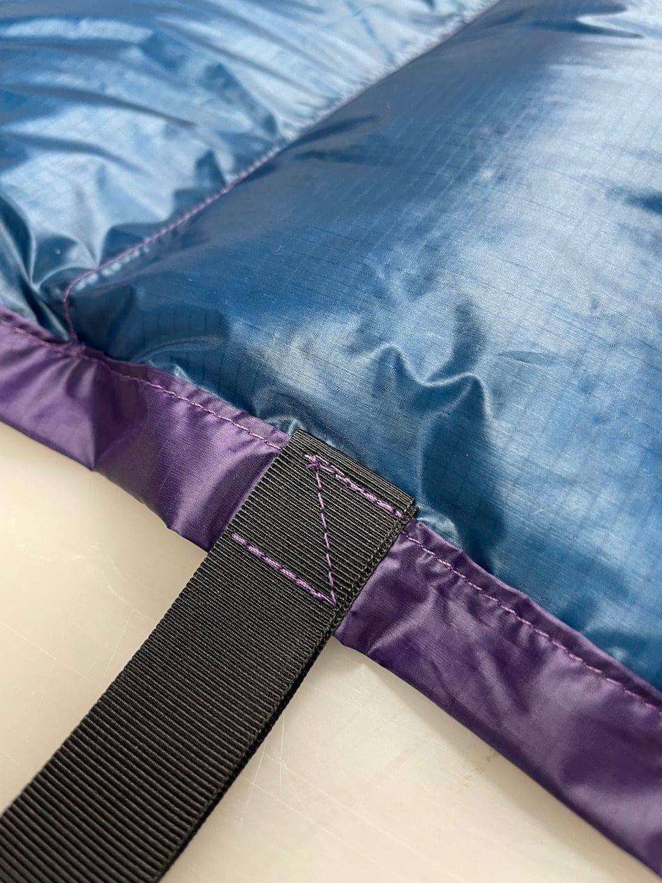 Close-up of a custom quilt's blue shell, purple edge binding, webbing strap, and contrast stitching