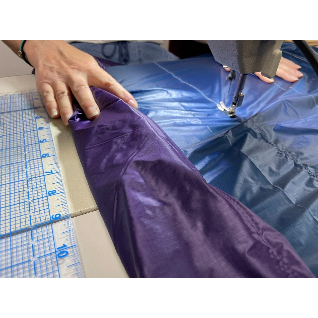 Hands guiding a purple and blue custom quilt through a sewing machine in the Jacks R Better Pennsylvania workshop