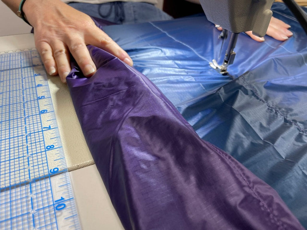 Hands guiding a purple and blue custom quilt through a sewing machine in the Jacks R Better Pennsylvania workshop