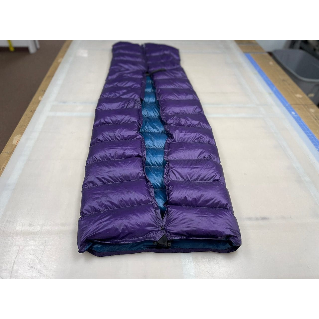 Custom ultralight backpacking quilt with a Purple shell and Moroccan Blue lining, formed into a foot box and laid full length on the workshop table