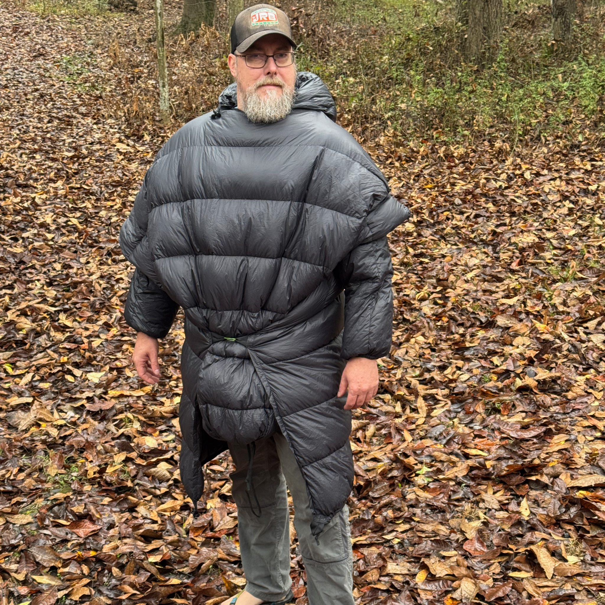 Man wearing the Sierra Stealth 40° wearable down quilt outdoors in autumn woods